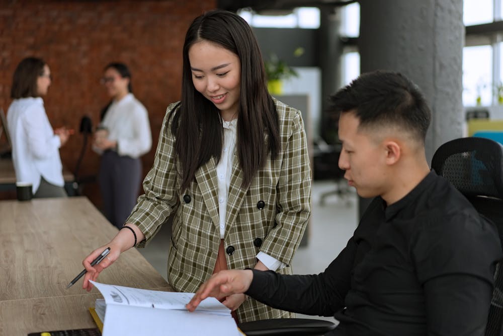 Two colleagues collaborating over a document at a desk in a modern office setting.